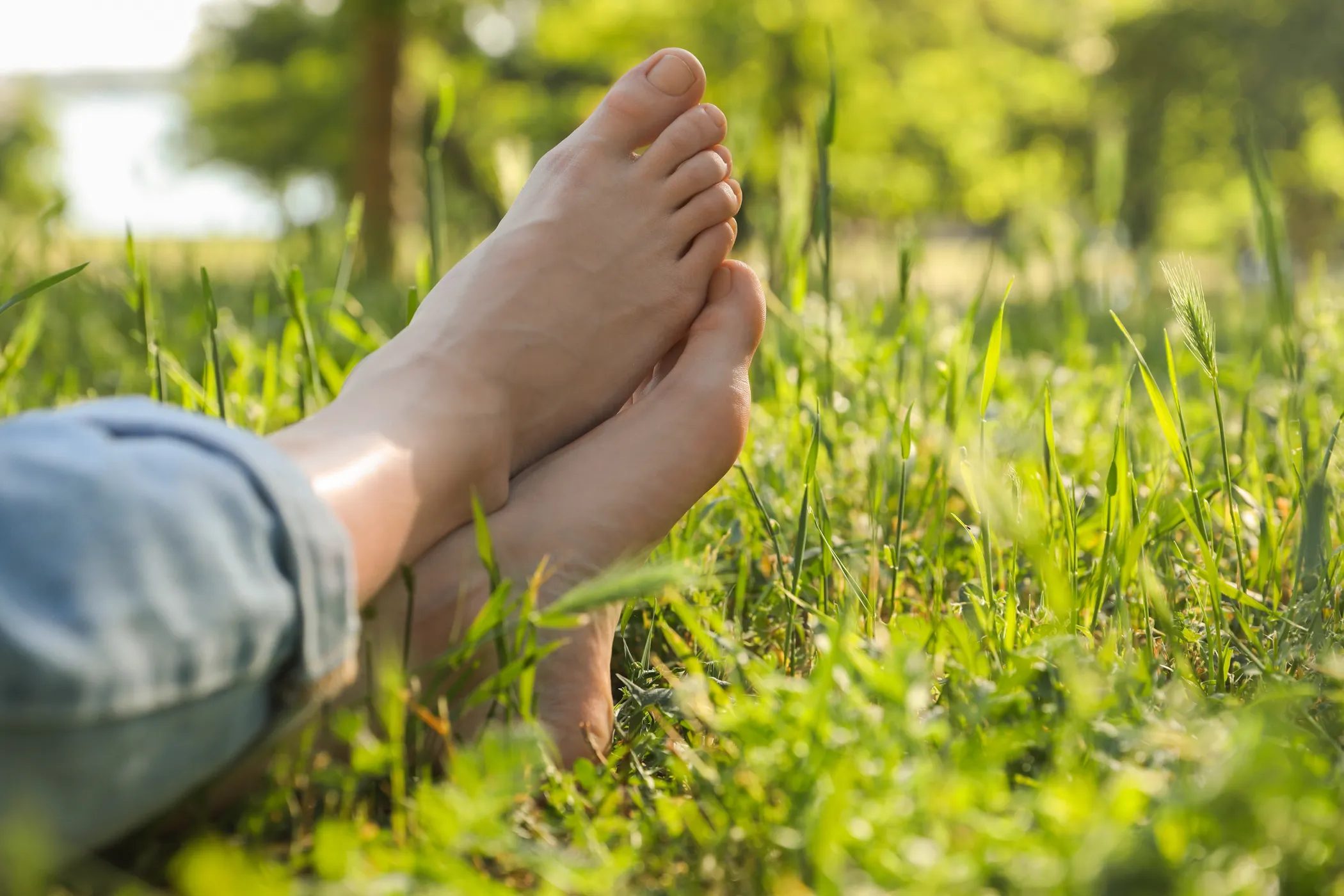 Barfüße liegen entspannt übereinander im sonnigen Gras.